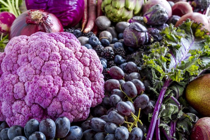 Arranjo de frutas e vegetais azuis e roxos, incluindo uvas, ameixas, bagas, cebola roxa e repolho roxo