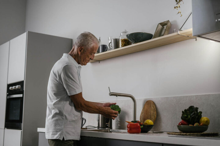 An elderly man washing broccolis and other vegetables