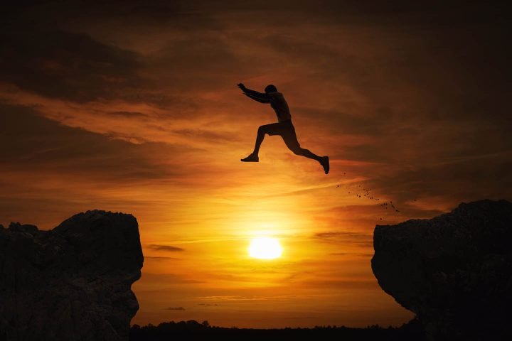 A courageous man jumping over a gap between two rocks