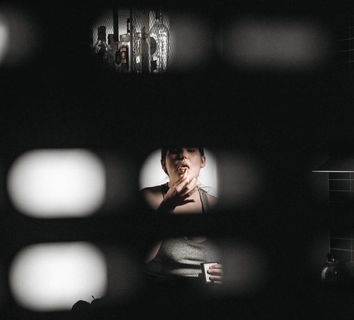 A woman eating secretly behind some blinds and being also addicted to alcohol