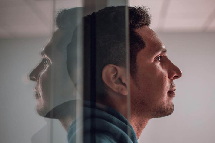 A man stepping out of a glass door, leaving the reflection of his face behind.