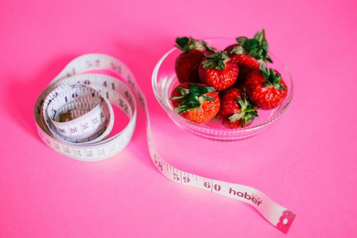 A bowl of strawberries with a measuring tape, depicting the diet concept.