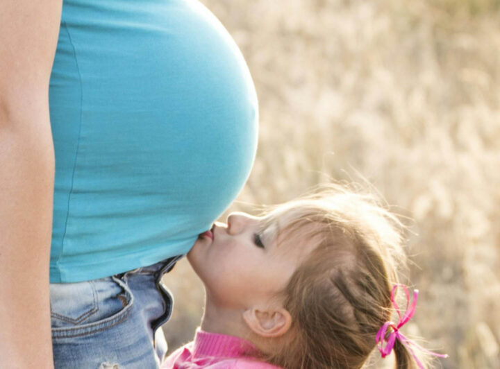 A pregnant woman with her daughter kissing the belly