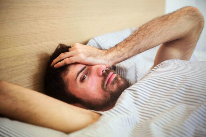 A man is lying in bed sick with a headache