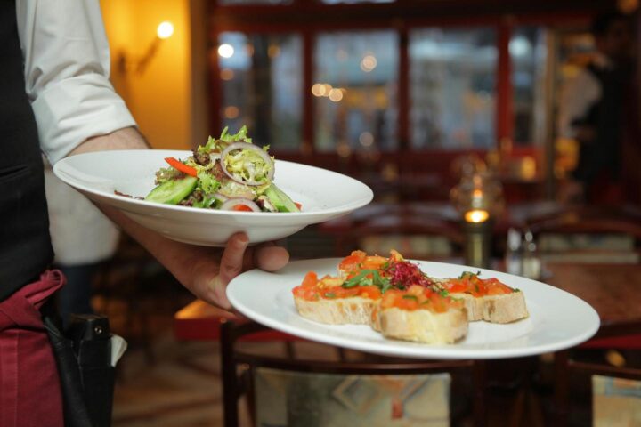 A waiter in the restaurant bringing a salad plate and veggie breads