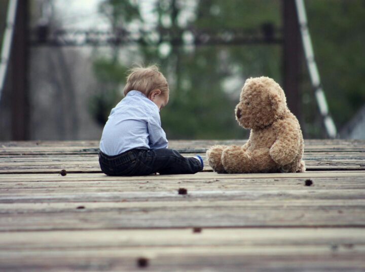 A teddy bear bein the friend of a toddler sitting on a bridge