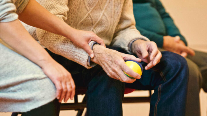 A woman holding the hand of her aged father