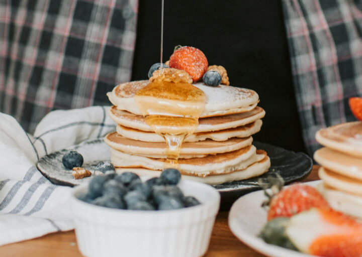 Pouring maple syrup over a stack of pancakes