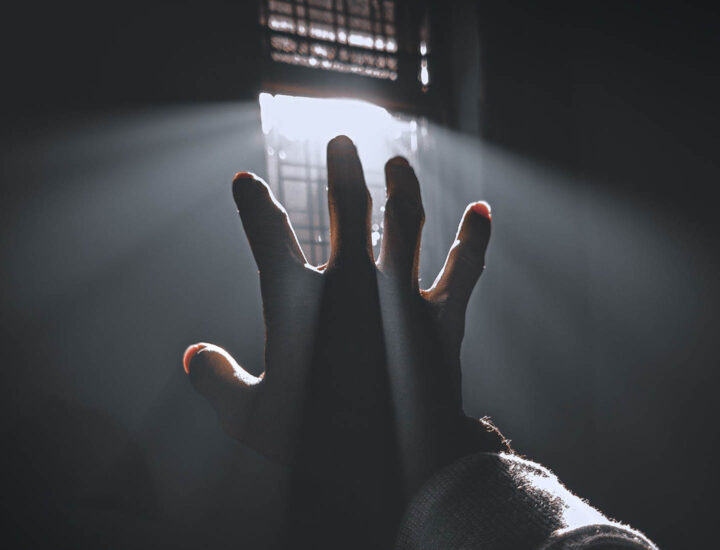 A hand reaching out after rays of light entering a window
