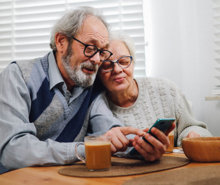 An elderly couple watching together images on the cell phone