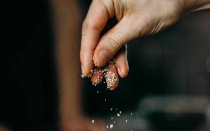 A hand sprinking a pinch of coarse salt over a dish
